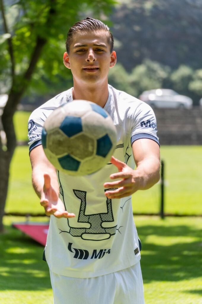 A young man in sportswear catching a soccer ball outdoors in a park on a sunny day.