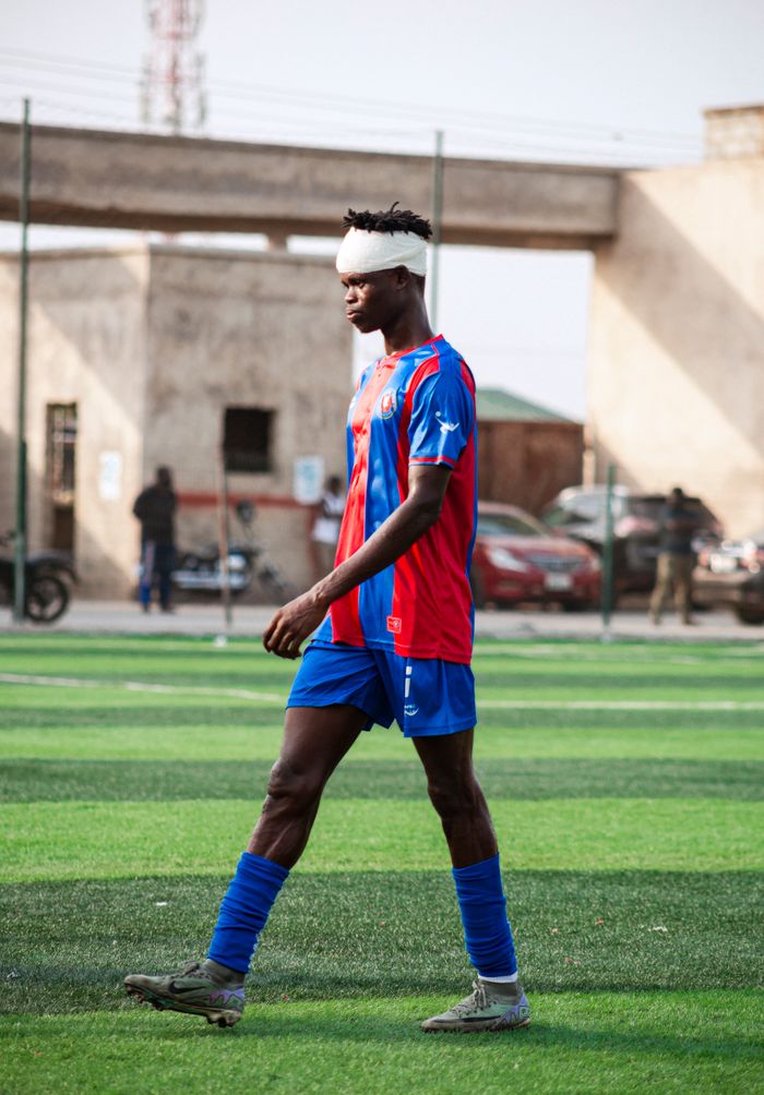A football player walks on a turf field with a head bandage and soccer gear.