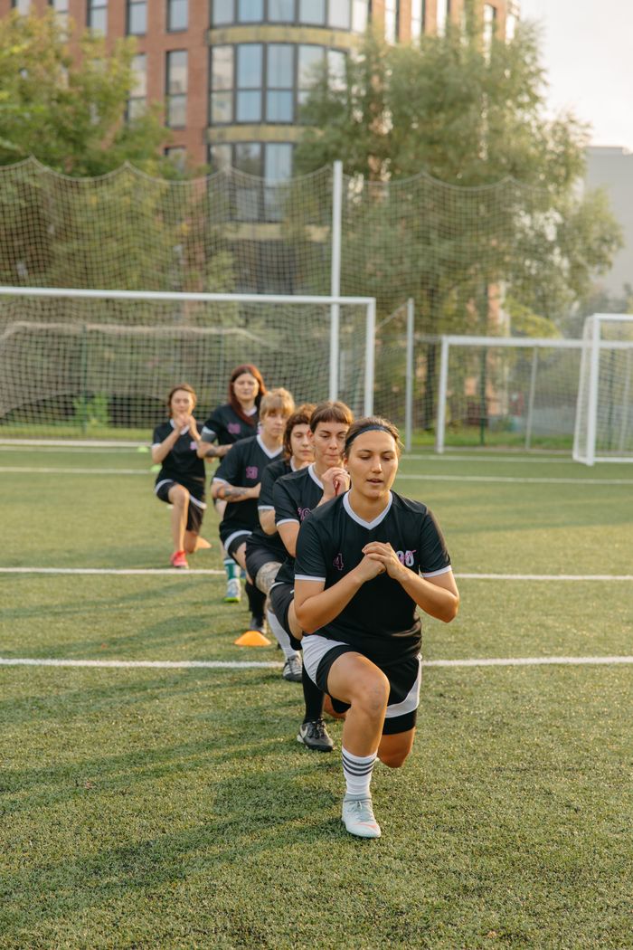 A line of female athletes performing drills on an outdoor soccer field.